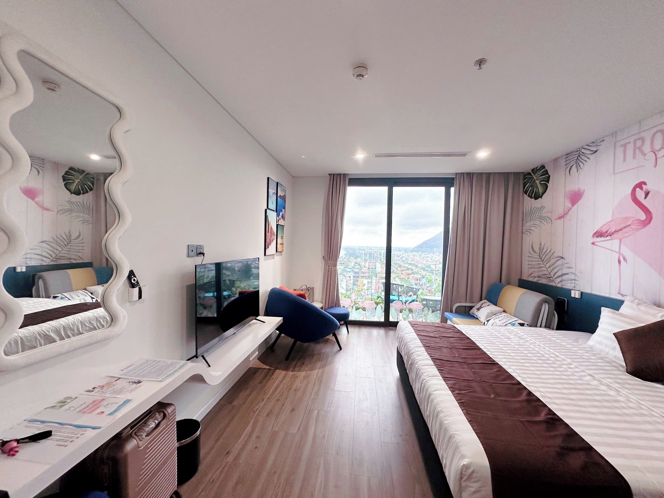 A modern hotel room with a large bed, a desk, a TV, and a city view.