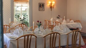 Comedor con varias mesas dispuestas para una comida, sillas de madera y una araña.