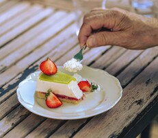 Una porción de pastel en capas con fresas sobre un plato blanco en una mesa de madera.
