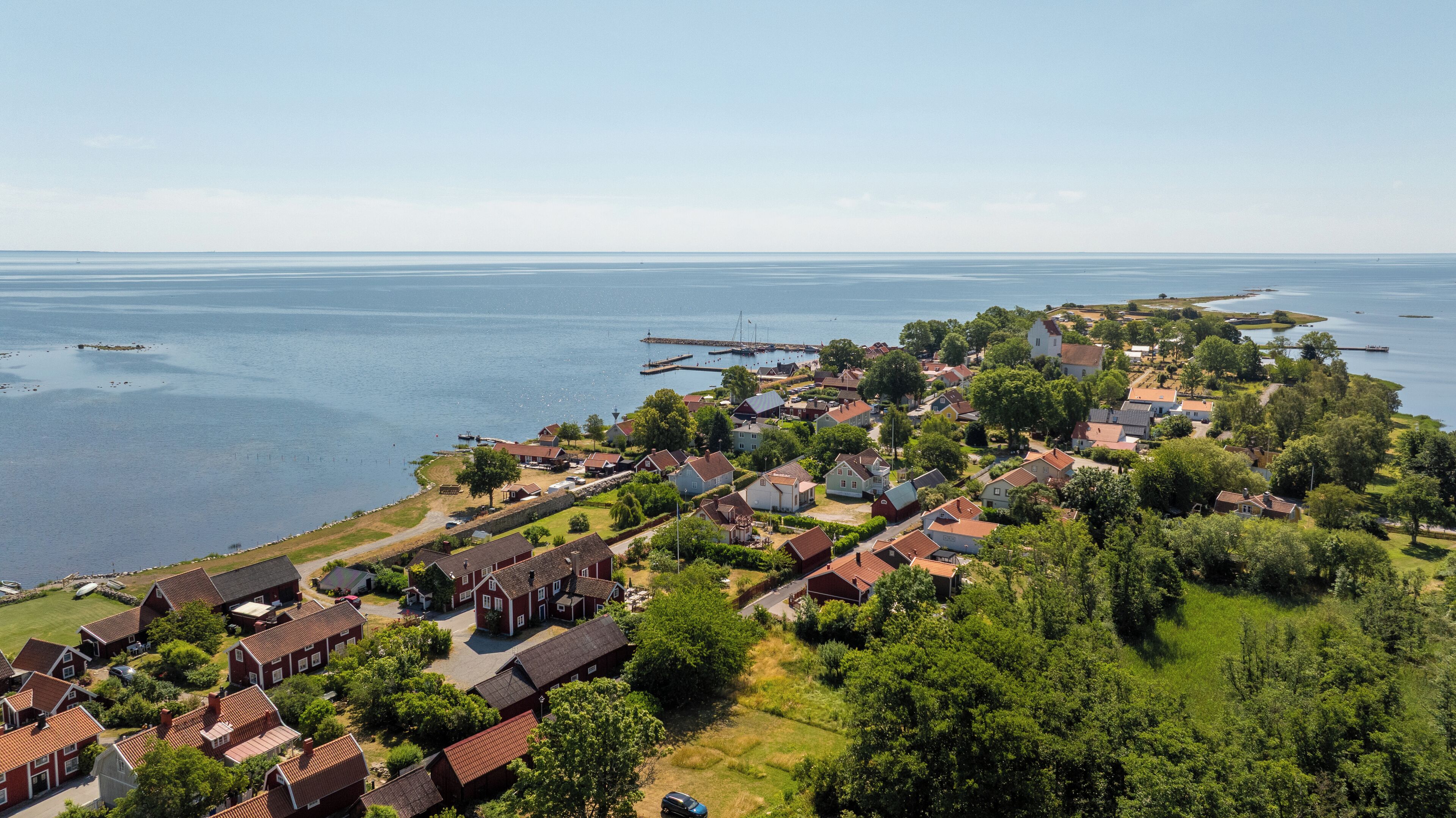 A coastal village with red-roofed houses, a dock, and a lighthouse.