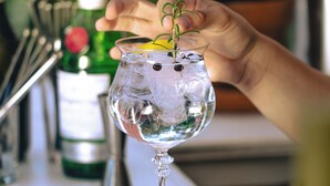 Una mano colocando un gajo de limón en un vaso con cubitos de hielo.