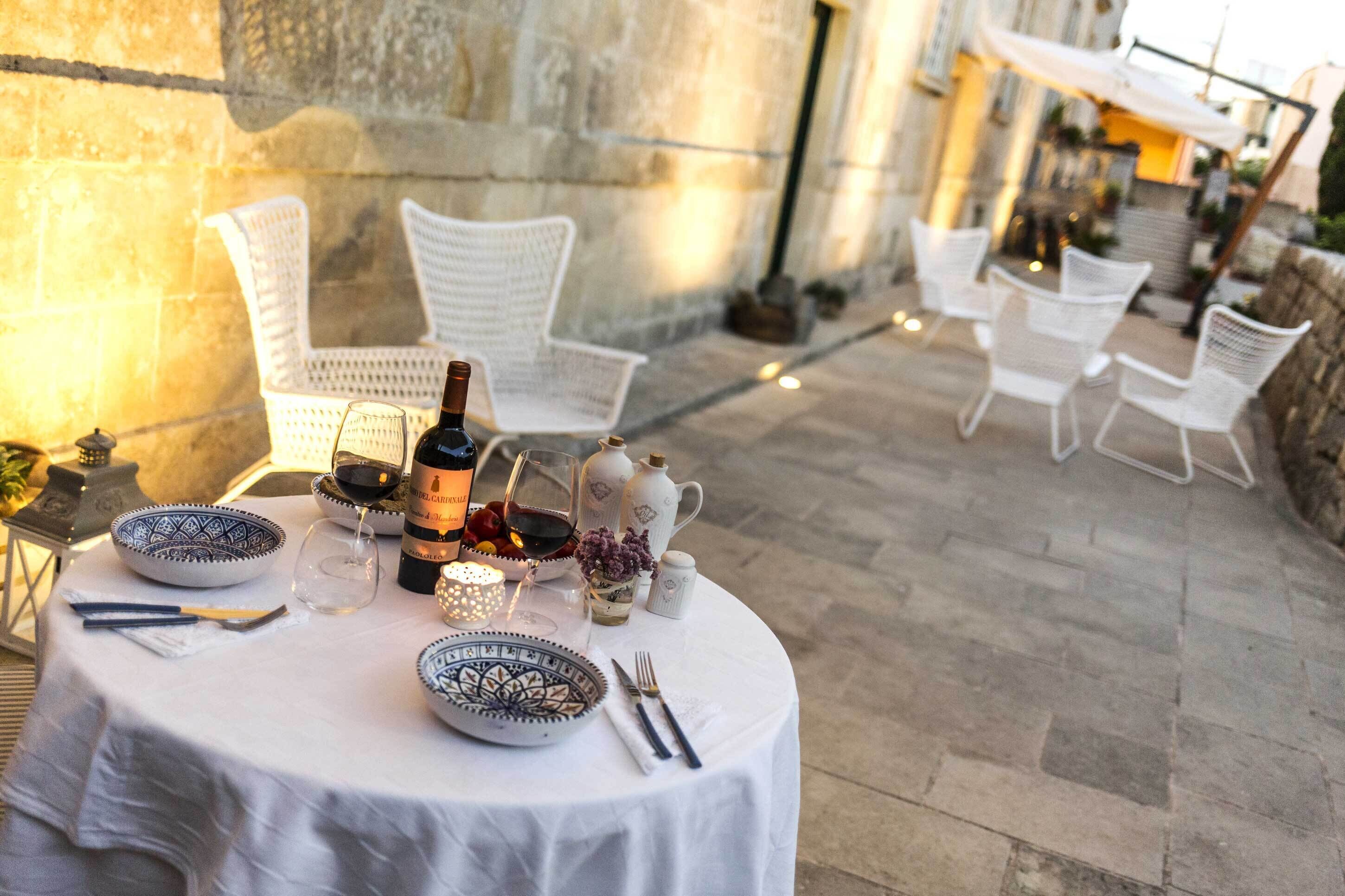 Un espace de restauration en plein air avec des tables rondes, des chaises en osier blanc et un mur en pierre en arrière-plan.