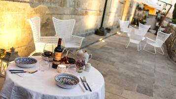 Un espace de restauration en plein air avec des tables rondes, des chaises en osier blanc et un mur en pierre en arrière-plan.