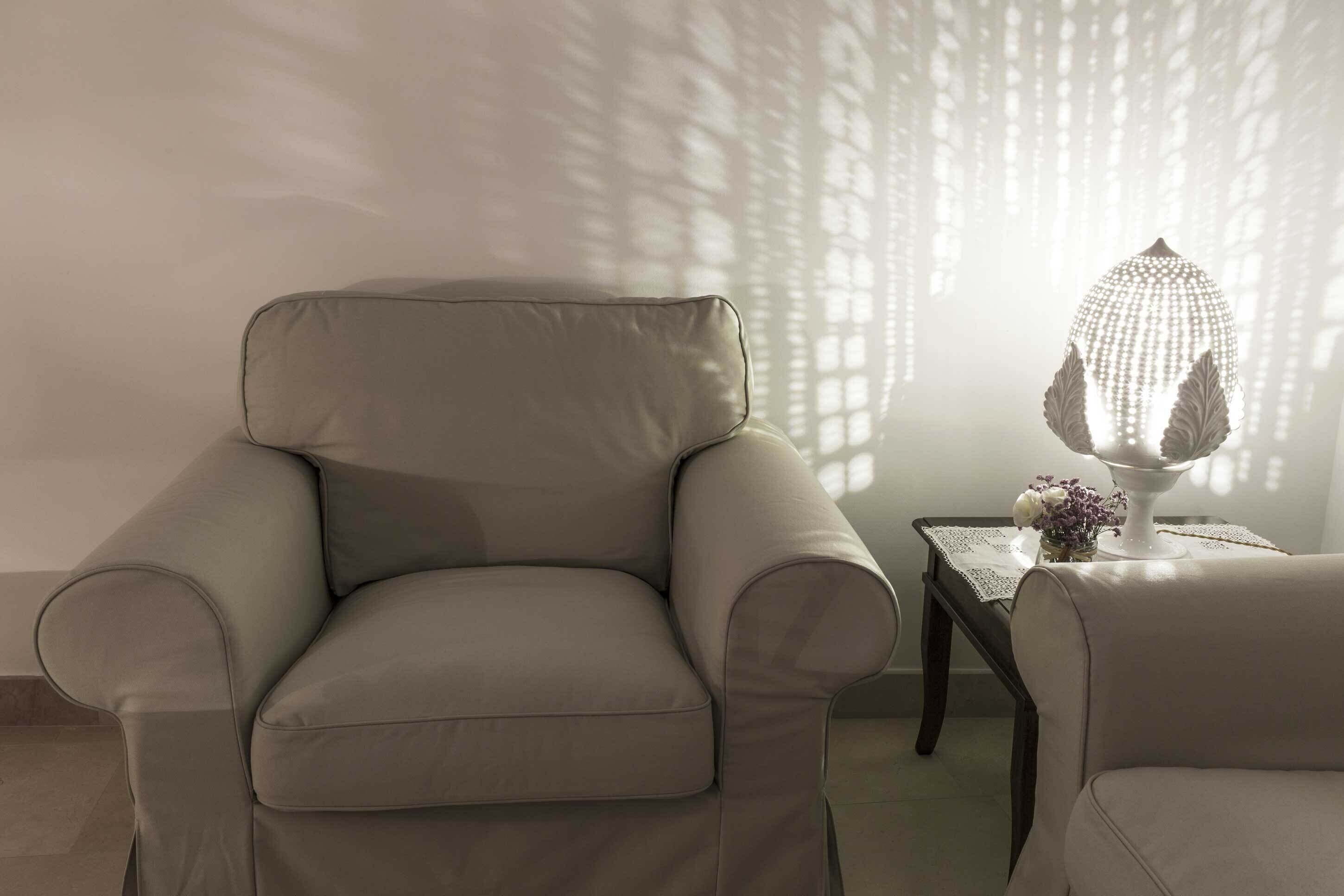 A modern living room with a leather armchair, a small table with a decorative lamp, and a wall with a patterned design.