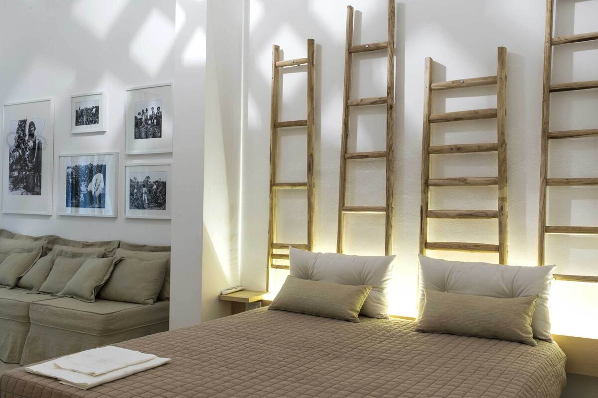 A neatly arranged bedroom with a bed, pillows, a nightstand, and a wooden ladder against the wall.