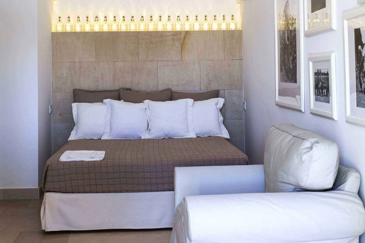 A bedroom with a large bed, a sofa, and a wall with framed pictures.