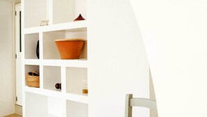 A white interior with a chair and a white shelving unit with various items. - Trapetum-Salento Domus by Oikia Vacanze (Cursi)