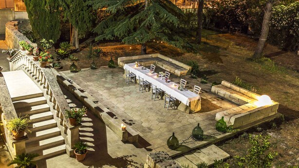 An outdoor patio with a long table set for dining, surrounded by potted plants and a stone wall. - Trapetum-Salento Domus by Oikia Vacanze (Cursi)