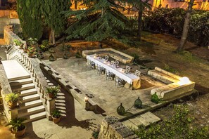 Eine Terrassensitzgelegenheit mit einem langen Esstisch, umgeben von Kübelpflanzen und einer Steinmauer.