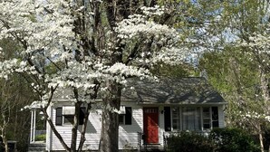 Une maison blanche avec une porte rouge, entourée d’arbres et d’herbe.