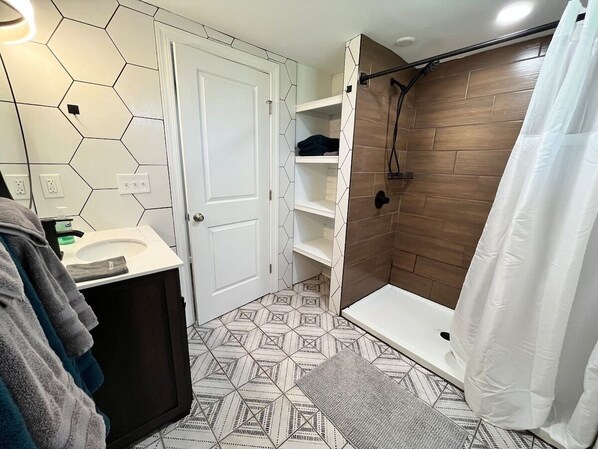 Un baño con un lavabo blanco, una ducha con pared de madera y un suelo de patrón hexagonal.
