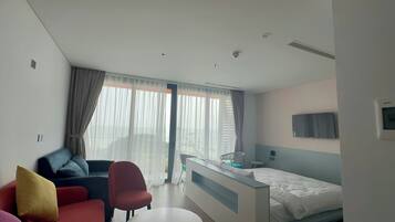 A hotel room with a bed, a desk, a chair, a couch, and a TV.