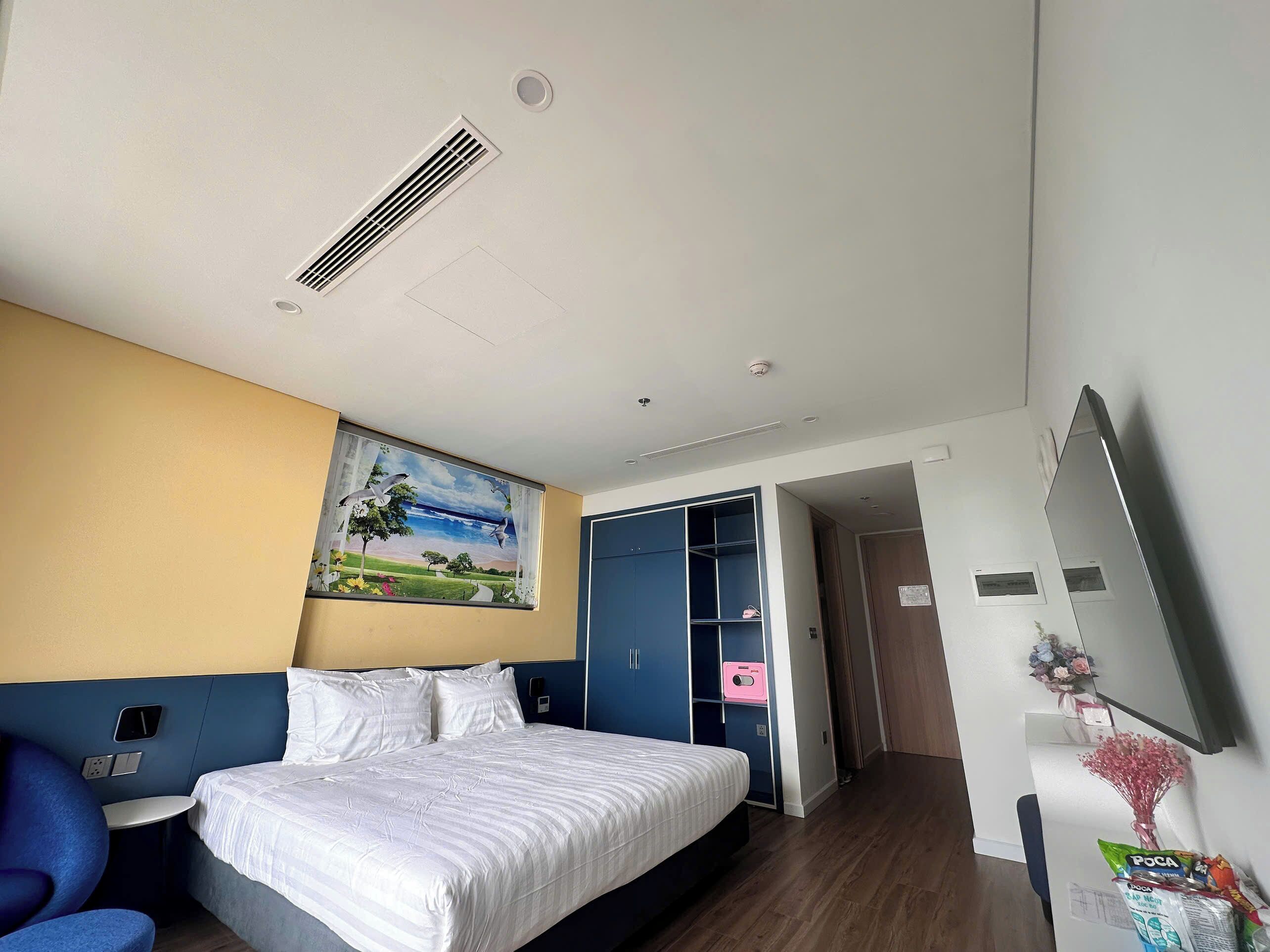 A hotel room with a bed, a desk, a chair, a painting, a wardrobe, and a mirror.