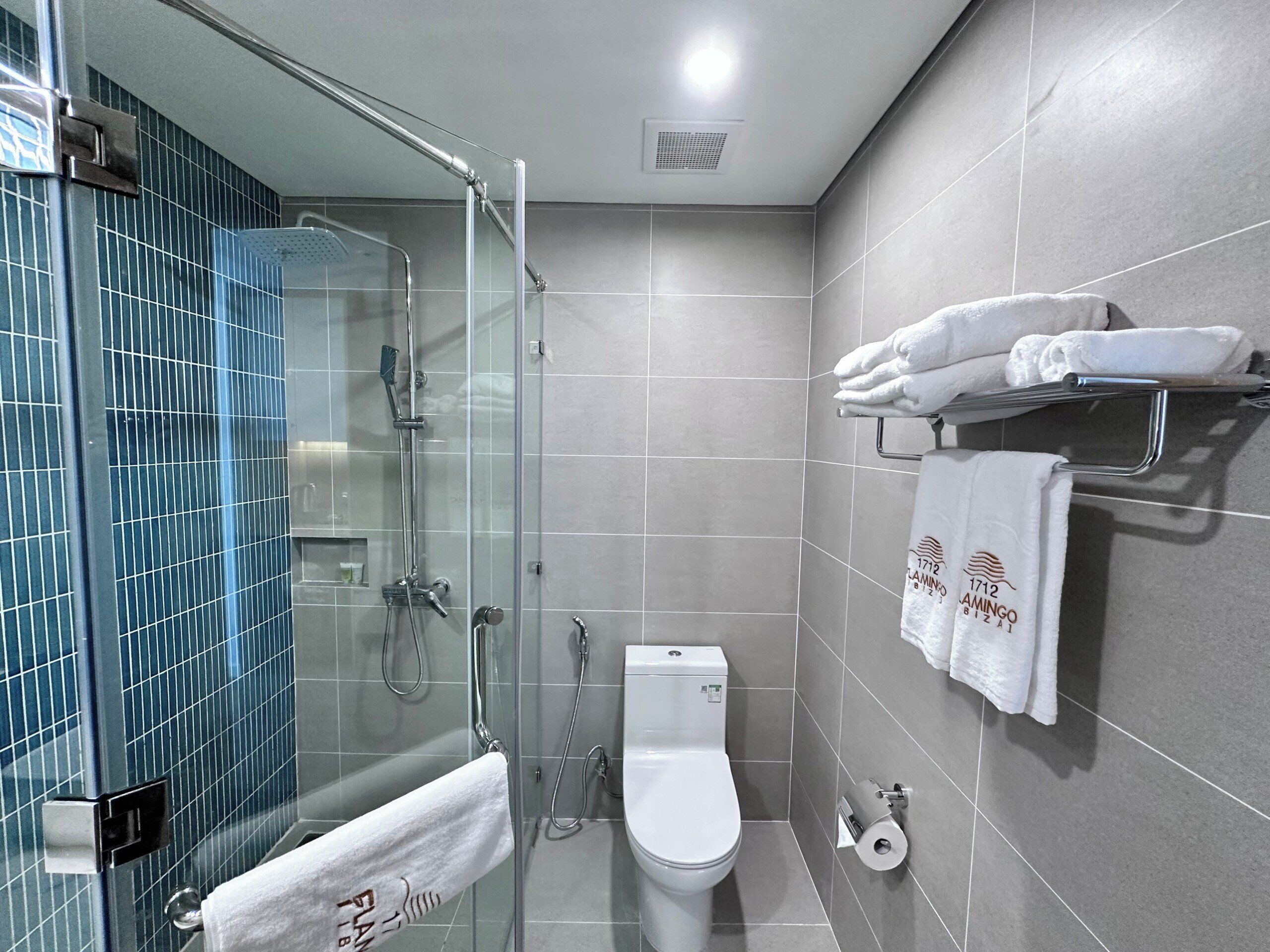 A modern bathroom with a glass-enclosed shower, a toilet, and a towel rack with neatly folded towels.