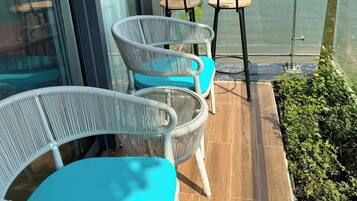 A balcony with wicker chairs and a small table, overlooking a body of water.