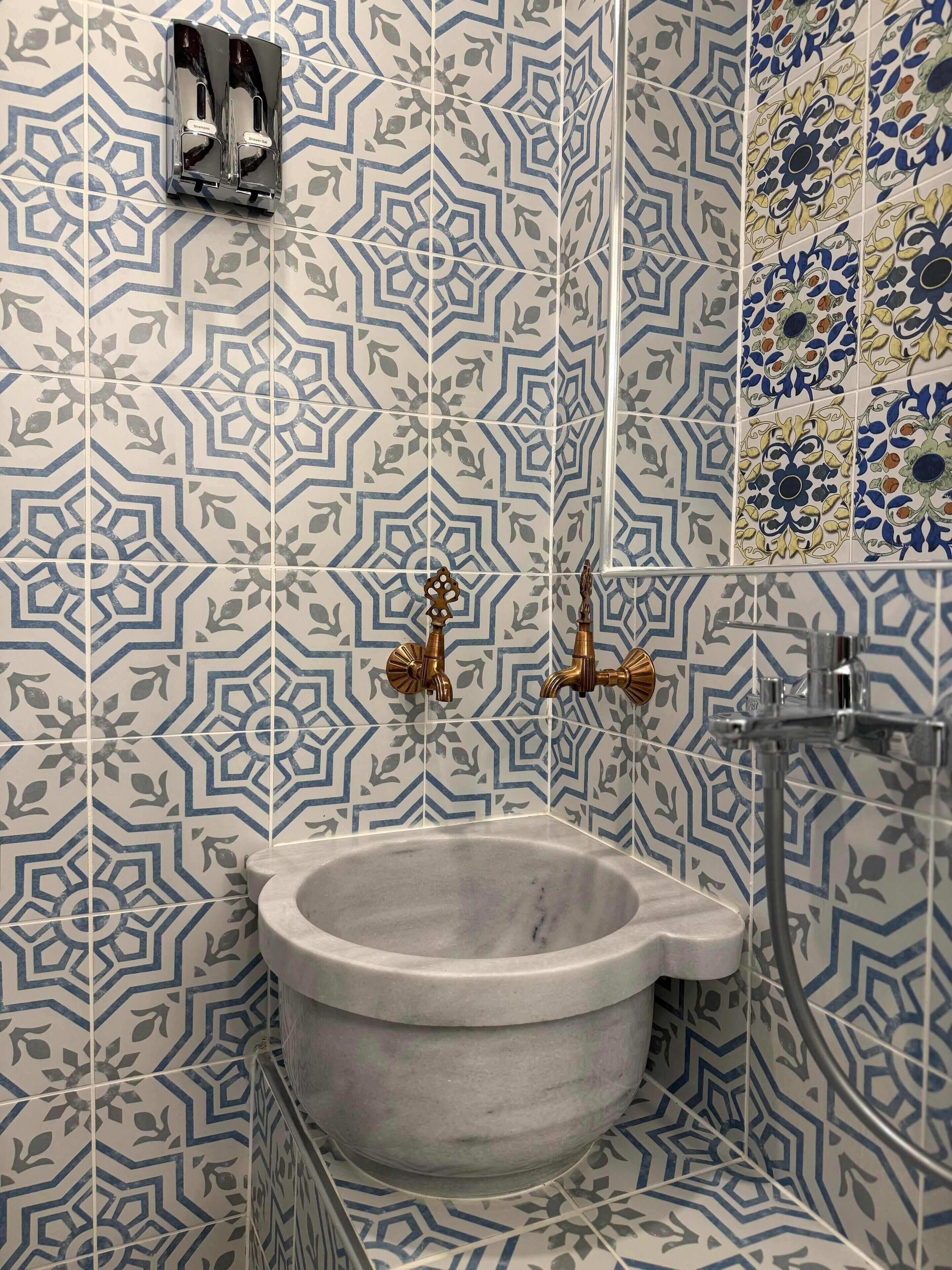 A bathroom with a geometric patterned tile wall, a marble sink, and brass fixtures.