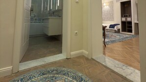 A spacious hallway with a large, ornate rug, leading to a bathroom with a glass shower and a sink. - Oasis Inn Budapest (Budapest)