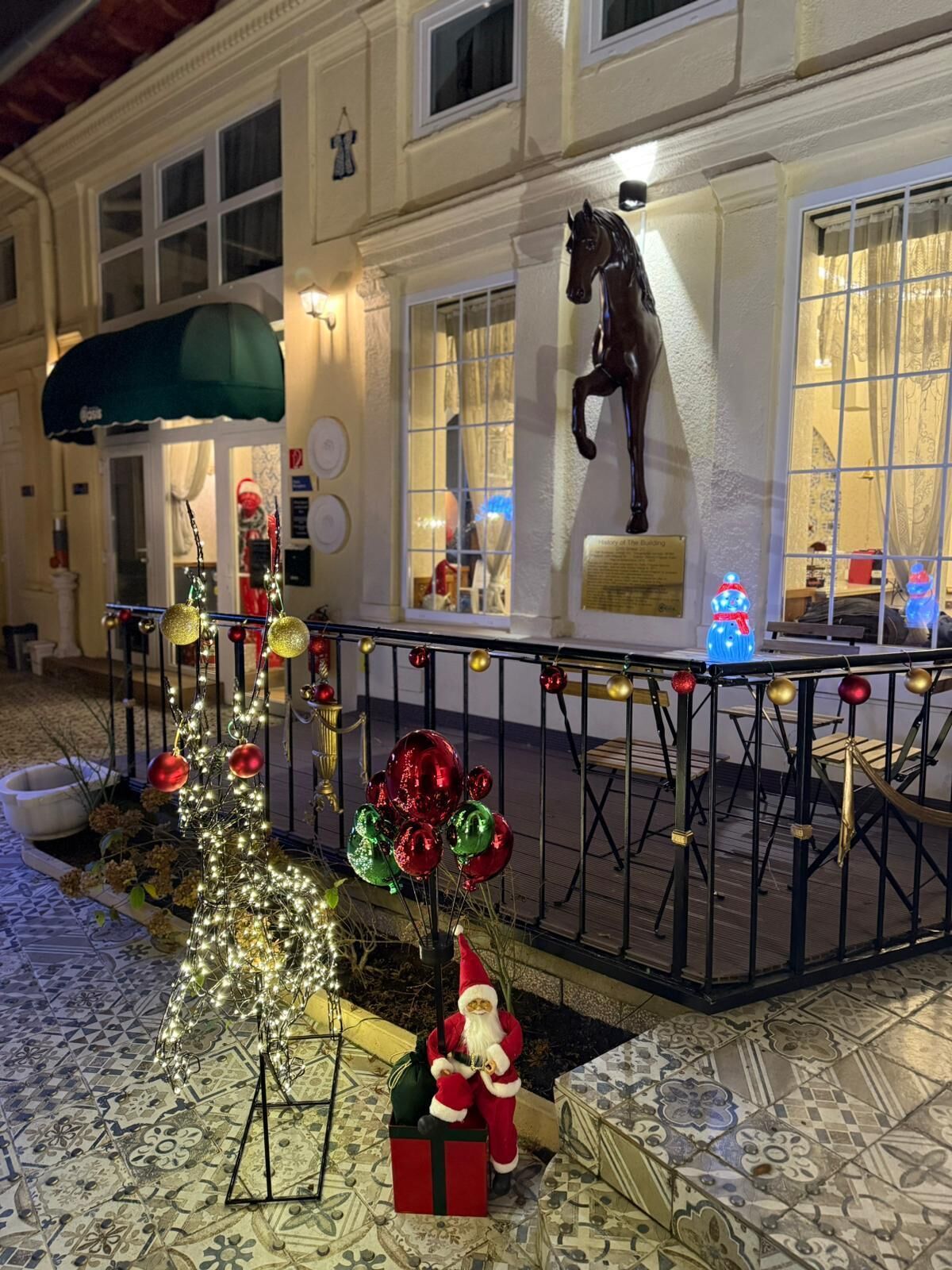 Un espace extérieur décoré avec un sapin de Noël, une statue du Père Noël et une statue de cheval.