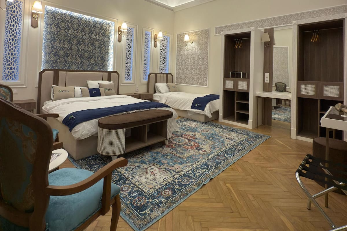 A hotel room with two beds, a desk, a chair, a small table, and a wardrobe.