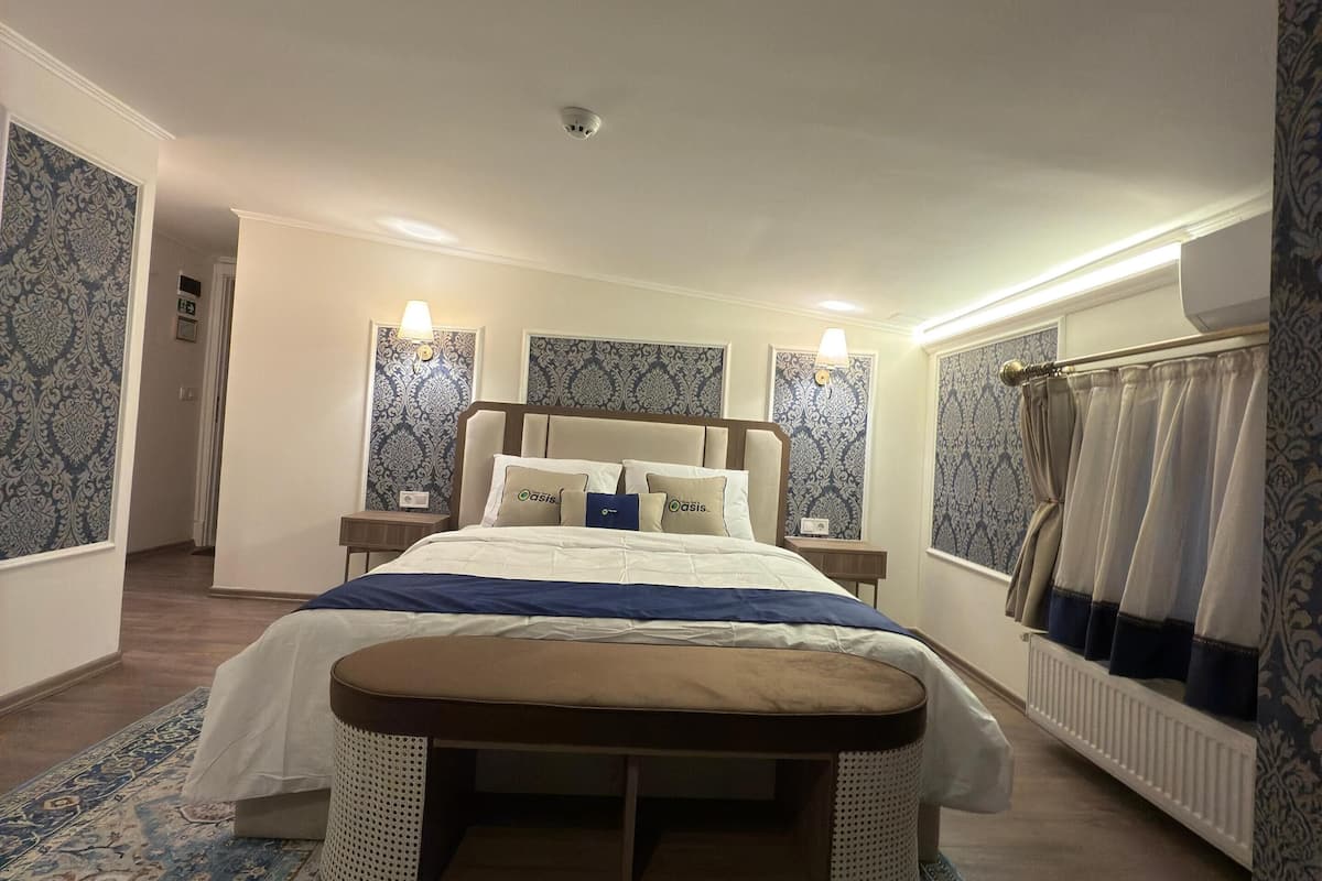 A bedroom with a large bed, bedside tables, a nightstand, a patterned rug, and a window with curtains.