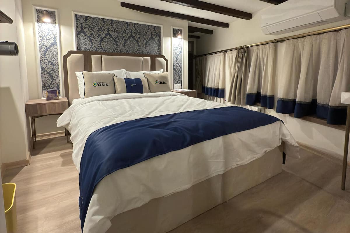 A bedroom with a large bed, a nightstand, a wall-mounted air conditioner, and patterned wallpaper.