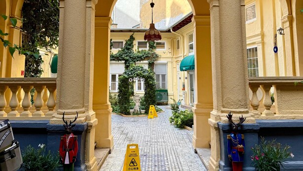 A hotel entrance with a yellow archway, a wet floor sign, and a doormat with the hotel logo. - Oasis Inn Budapest (Budapest)