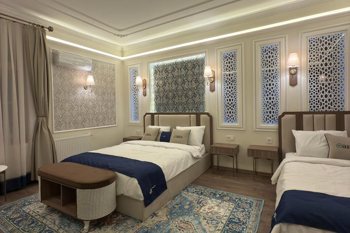 A modern hotel room with a large bed, a smaller bed, a bench, and a patterned rug.