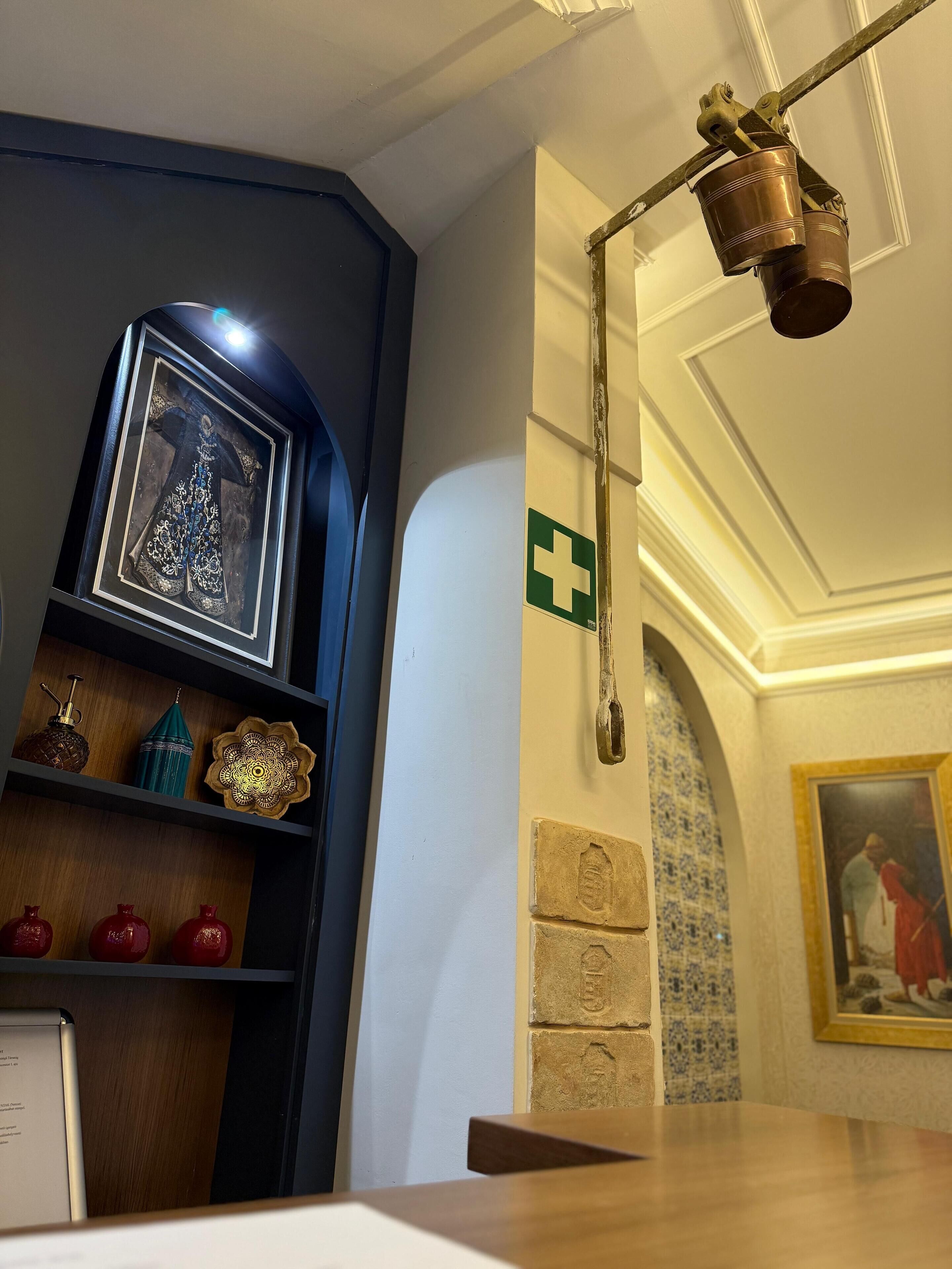 A room with a framed picture on a shelf, a green cross sign on the wall, and a painting on the wall.