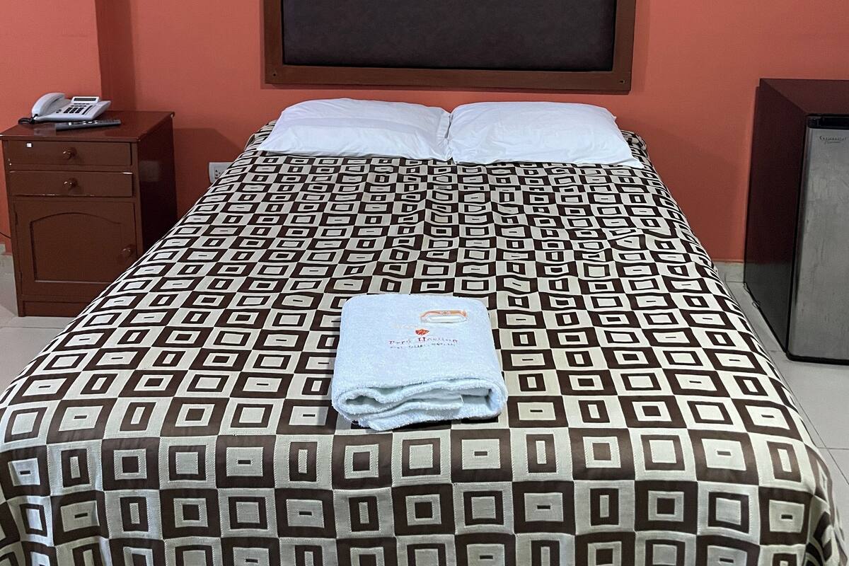 A neatly made bed with a patterned bedspread, a folded towel, and a bedside phone on a nightstand.
