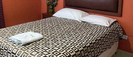 Una habitación de hotel con una cama, una mesita de noche, un aire acondicionado y una planta en maceta.