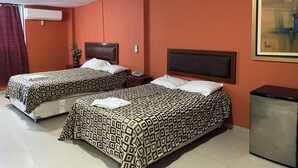 A hotel room with two beds, a small bedside table with a lamp, a wall-mounted air conditioner, and a painting on the wall. - Hoteles Perú Hosting (Piura)