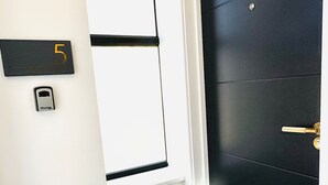 A door with a black panel and a brass handle, a white wall with a black mailbox, and a small mailbox with a key on the wall.