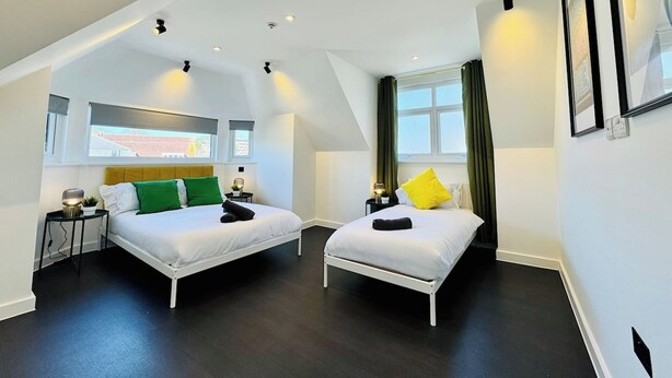 A modern hotel room with two beds, a large window, and a ceiling with recessed lighting.
