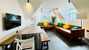 A modern loft apartment with a dining area, a sofa set, and a TV mounted on the wall.