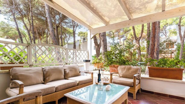 Eine Terrasse im Freien mit Korbmöbeln, einem Glastisch und Blumentöpfen.