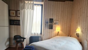 Un dormitori amb un llit gran, una cadira, un radiador i una finestra amb cortines.