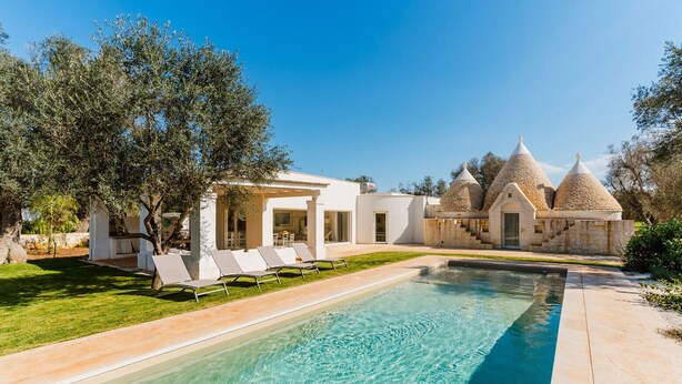 A modern villa with a swimming pool, outdoor seating, and unique conical stone structures.