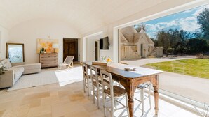 A spacious living room with a large window, a wooden dining table, and a cozy seating area.