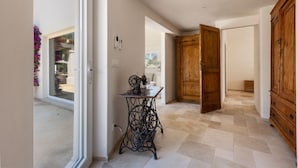 A hallway with a sewing machine, wooden doors, and a view to the outside.