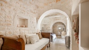 A stone-walled room with a wooden bed, a small table, and a bench.