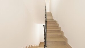 Una escalera con peldaños de madera y barandilla metálica, que lleva a una puerta en la parte superior.