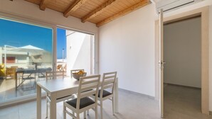 Un comedor con mesa y sillas, un ventanal grande y una puerta abierta que da a otra habitación.