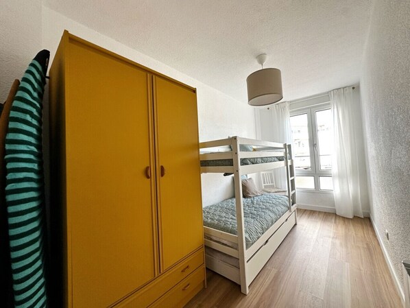 A bedroom with a bunk bed, a yellow wardrobe, and a window with curtains.