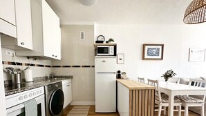 A compact kitchen with a microwave, oven, and washing machine. There is a dining area with a table and chairs. - Tierruca Green 30023 (Somo)