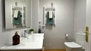 A modern bathroom with a white sink, a mirror, a toilet, and a towel rack. - Tierruca Green 30023 (Somo)
