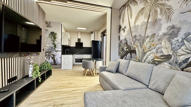 Una sala de estar moderna con un sofá gris, un televisor de pantalla plana y un comedor con una mesa pequeña y sillas.