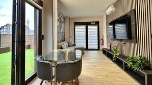 Una sala de estar moderna con una mesa de comedor de vidrio, un sofá y un televisor montado en la pared.
