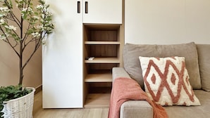 Un salon moderne avec un canapé gris, un coussin décoratif à motifs, une petite armoire en bois et une plante d’ornement.