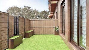 Une cour avec une pelouse artificielle, une clôture en bois et un bâtiment doté de grandes fenêtres et d’un balcon.