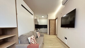 Un salon moderne avec un canapé gris, un téléviseur à écran plat fixé au mur et un plancher en bois.